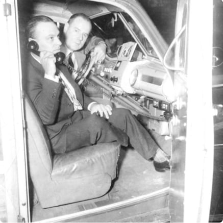 Man on passenger seat of open doored car with early mobile telephone