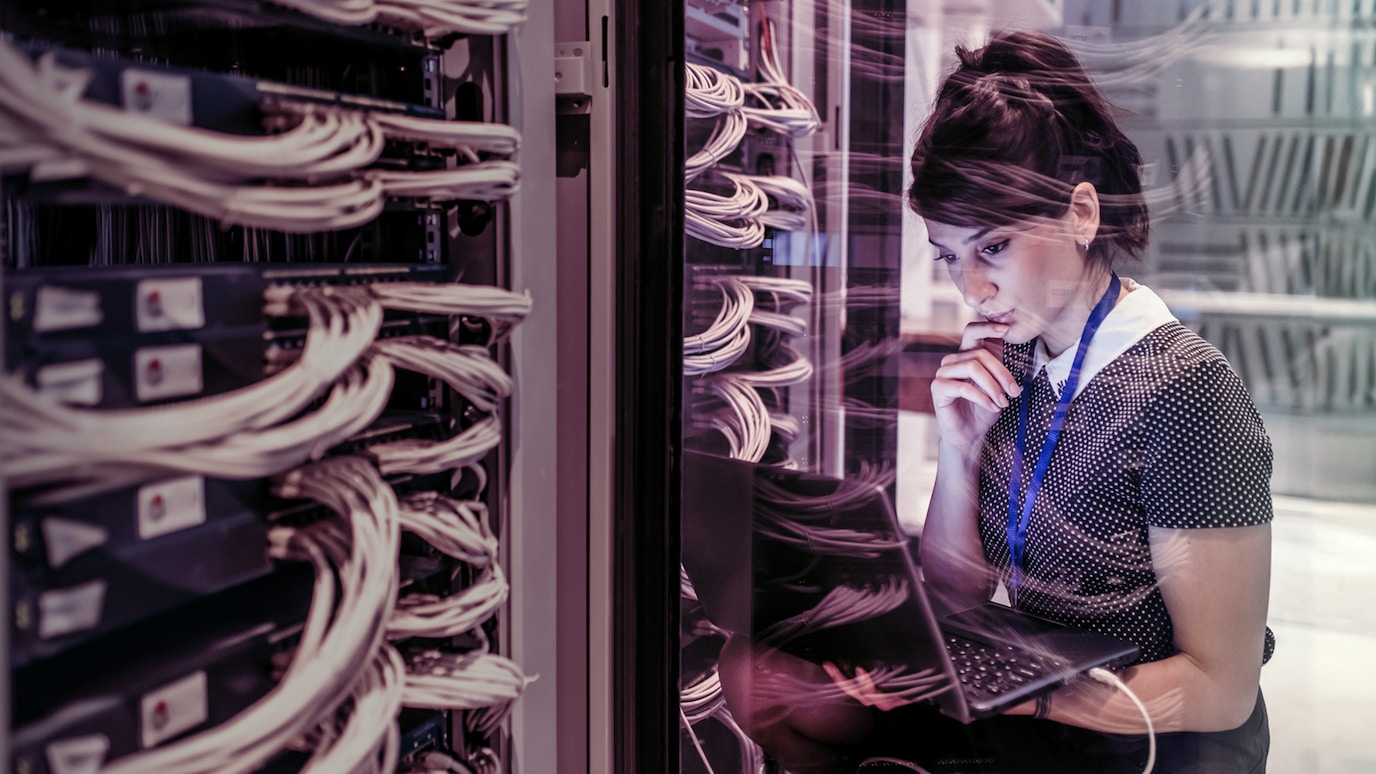 Technician studying laptop connected to server rack