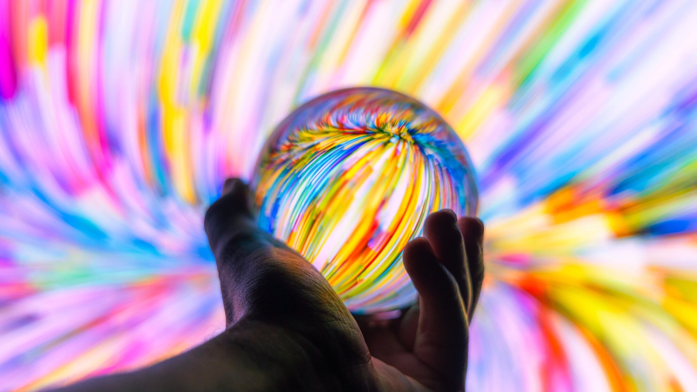 A ailhouette of a hand holding a see-through sphere against a coulourful background.